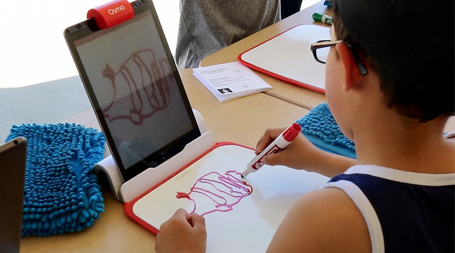 young boy drawing on paper as screen captures his art digitally