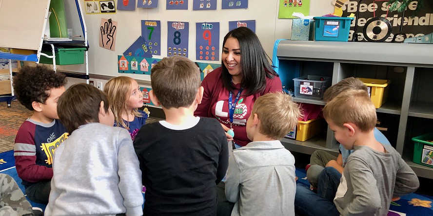 female teacher sits on floor with preschool boys and girls sitting around her