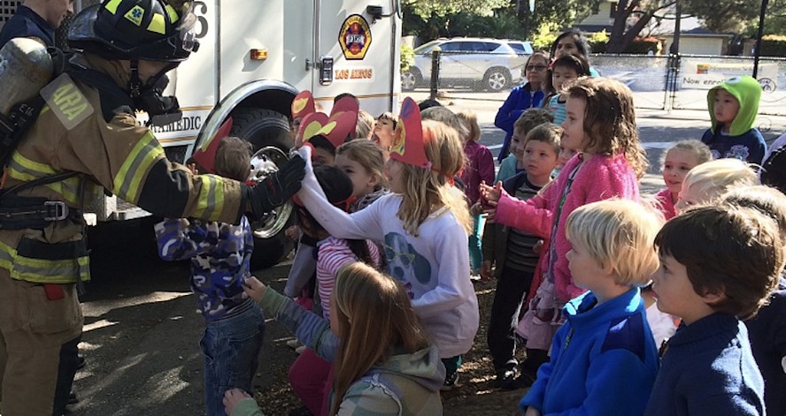 children gather around a firefighter as he shows them the fire truck