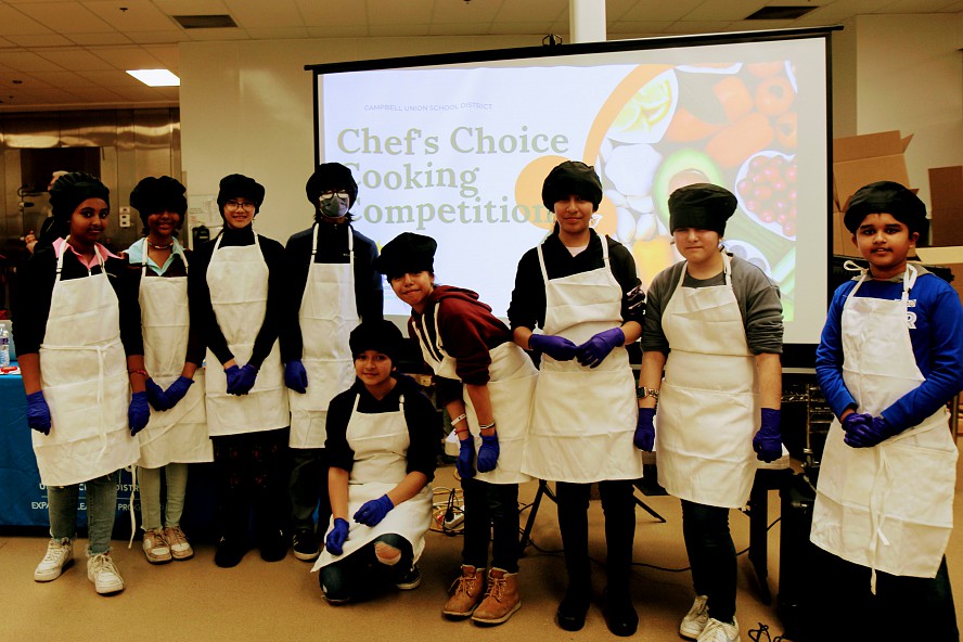 students wearing chef hats and aprons line up before the cooking competition