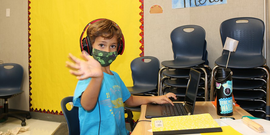 young boy with mask waves hello