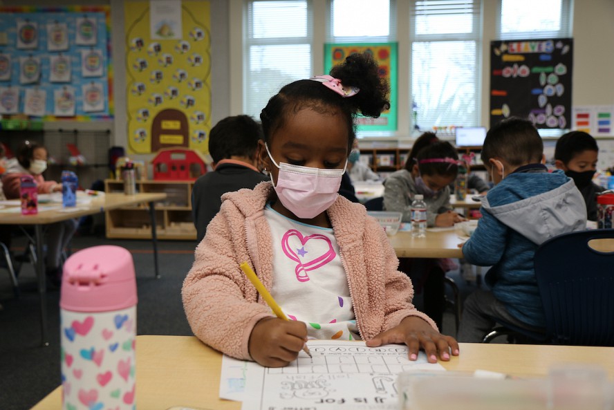 little girl in mask doing school work in class