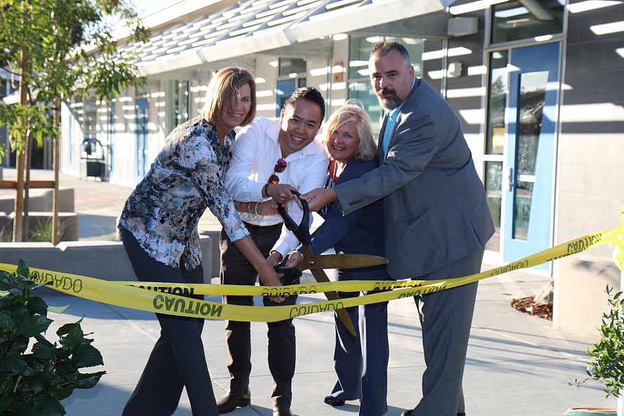 four adults cutting a ribbon made of construction tape with oversized scissors
