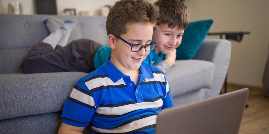 two boys smiling while looking at a laptop