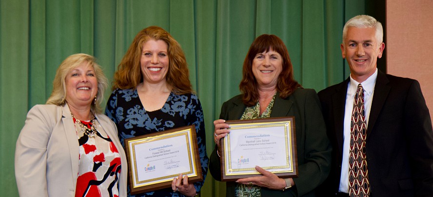four smiling people standing; two with awards