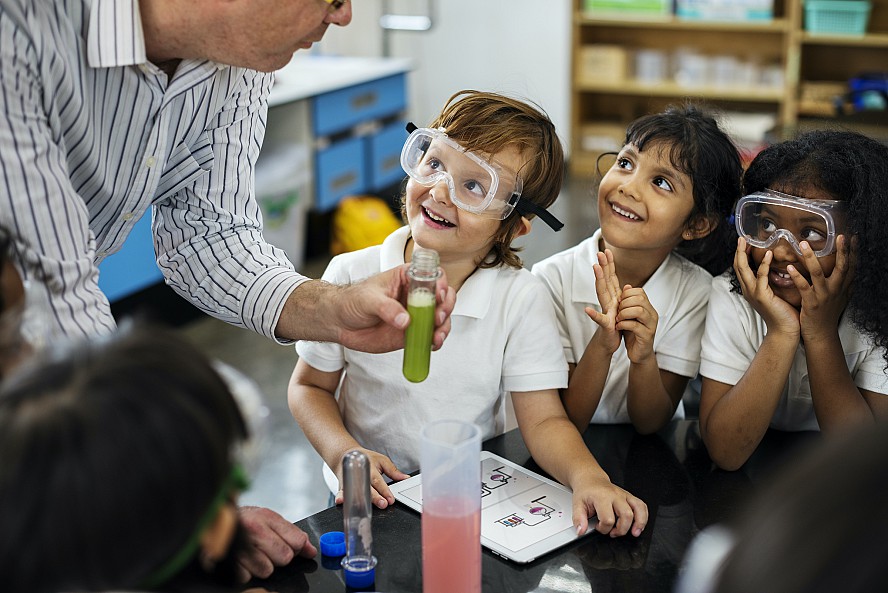 three young students smiling as adult demonstrates experiment