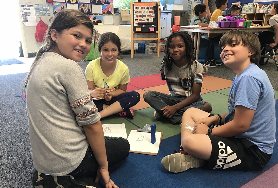 4 students sitting on floor, smiling at camera