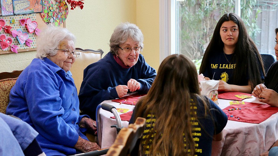 students work at table with elderly women