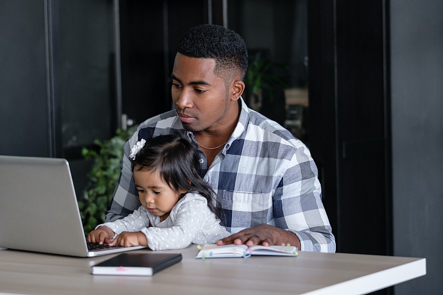 father with preschool girl on lap reaching for computer