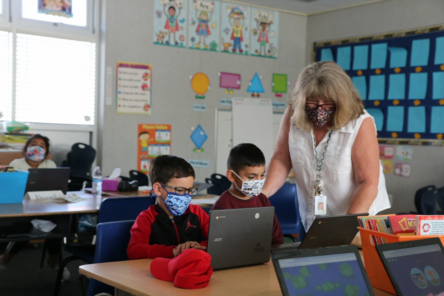 teachers assists students. All wearing masks.
