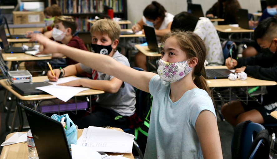 masked middle school girl raising hand in class