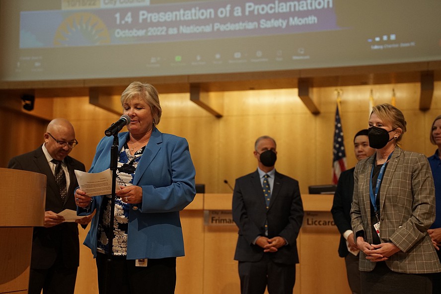 woman at podium. People standing behind her listening.