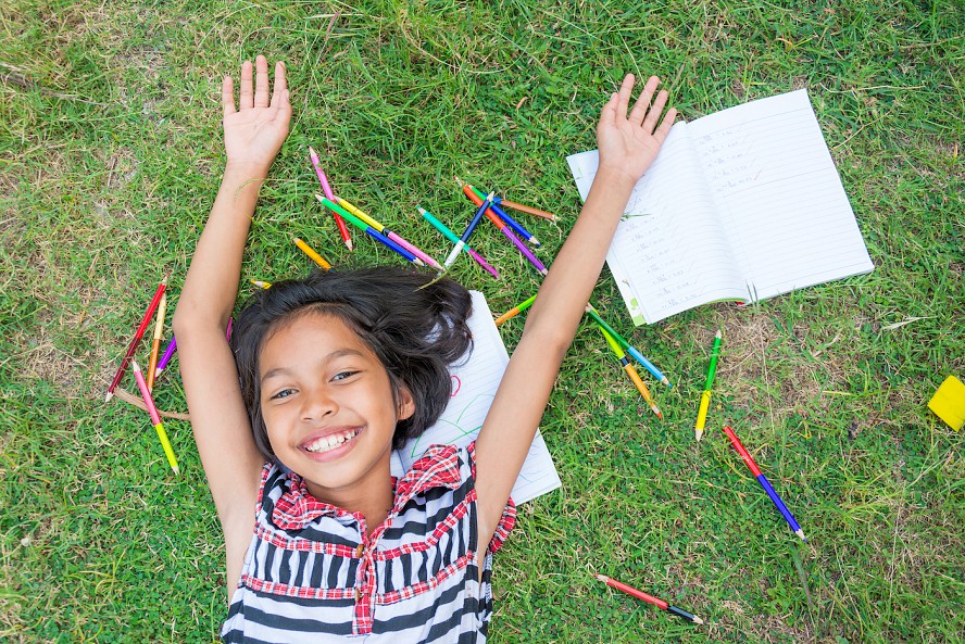 smiling girl in grass with crayons and paper