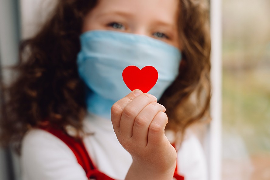 young girl wearing face mask holding a red heart sticker