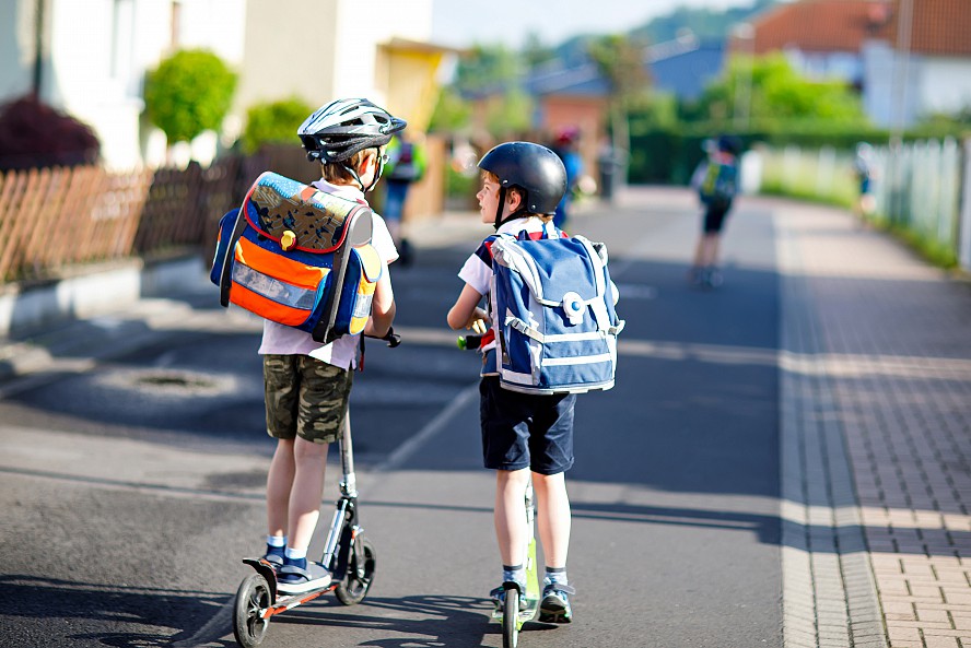 two boys with backpacks on scooters