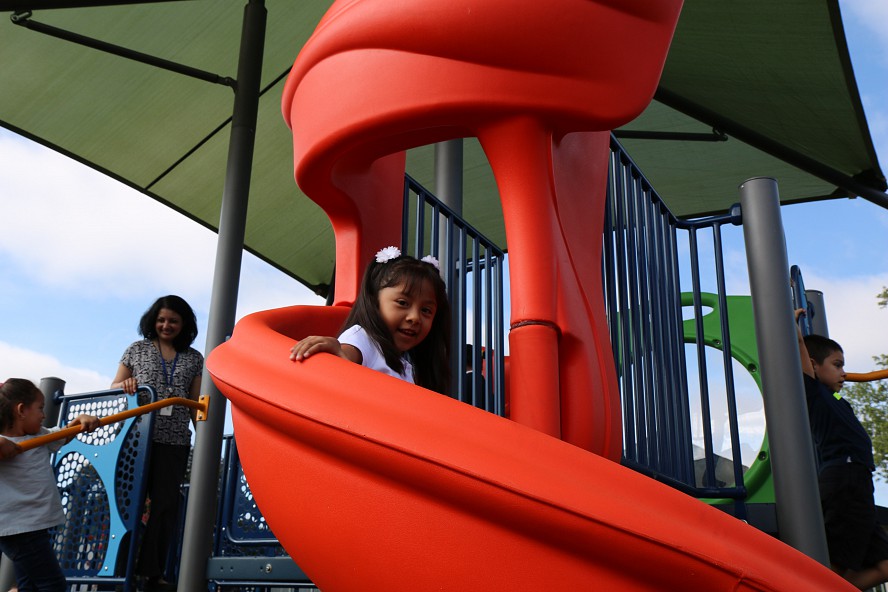 child goes down slide as adult supervises play