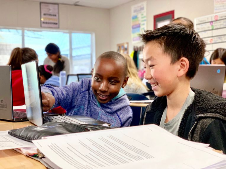 TWO BOYS WORKING AT COMPUTER AND SMILING