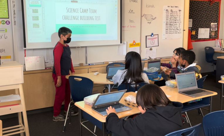 boy stands at front of class as other students watch