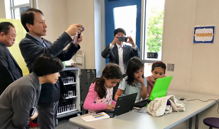 three girls work on laptops as adults take pictures