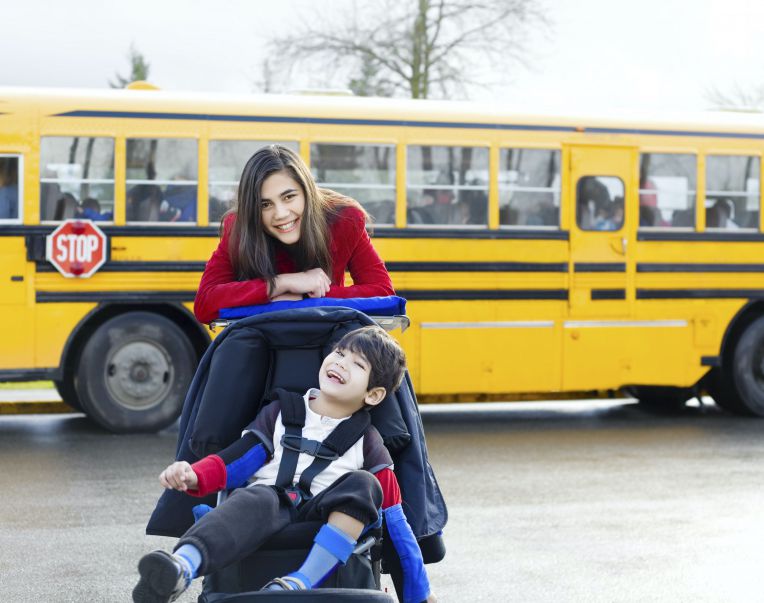 boy in wheelchair with big sister near school bus