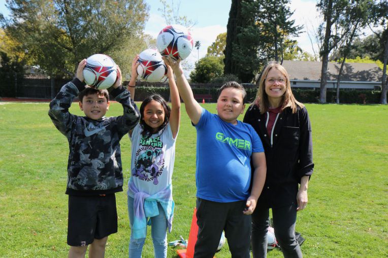two boys, one girl one female teacher all holding soccer balls