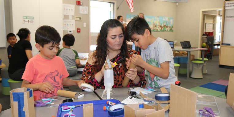 woman works with two boys creating things with tape and cardboard