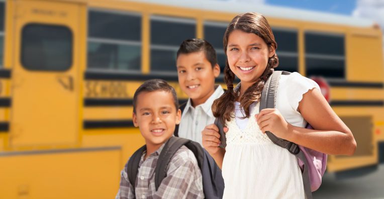 three smiling students near school bus