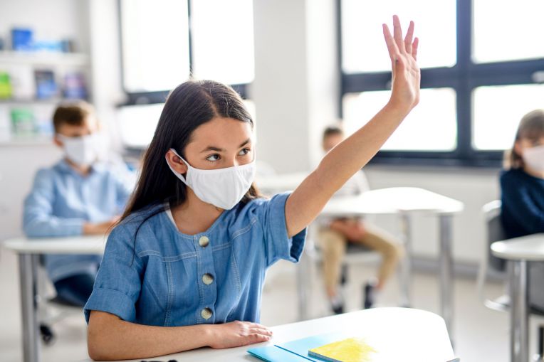 girl wearing mask raising hand in class